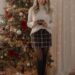 Woman wearing plaid skirt and cozy sweater standing in front of decorated Christmas tree
