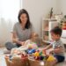 Mom sitting on the living room floor organizing toys into baskets while toddler plays nearby, creating a calm and clutter-free space.