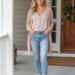 Woman in her 30s wearing light wash jeans, a neutral blouse, and a lightweight cardigan on a front porch with spring flowers.